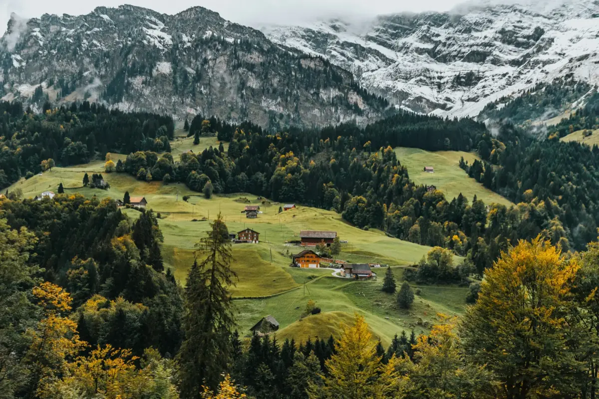 Schweizer Voralpenlandschaft mit verschneiten Bergen, Almwiesen und traditionellen Holzhäusern